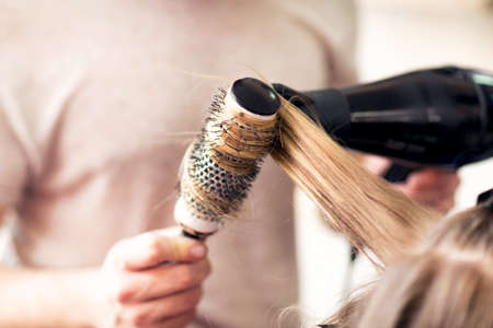 Working with comb and hair dryer at beauty salon close up