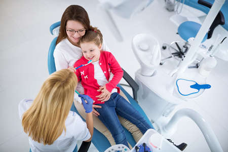 Young female dentist showing girl and her mom how to wash teeth