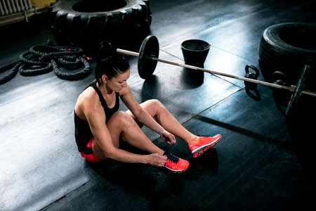 Female fit girl resting and bins sneakers and prepare for exercise at gym