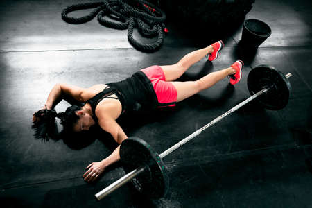 Tired young woman after hard training lying near weights