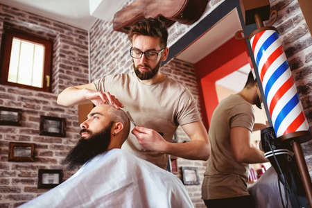 Professional master hairdresser shaves client head in barbershop salonの写真素材