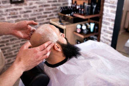 Professional Master hairdresser shaves client head in barbershop salonの写真素材