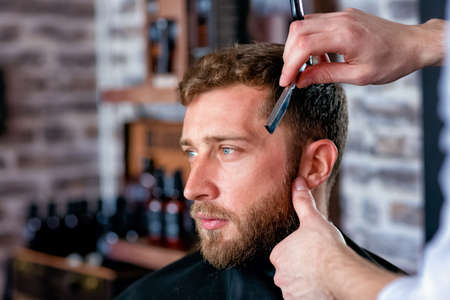 Hairdresser shaves man's beard with a blade in a male barber shopの写真素材