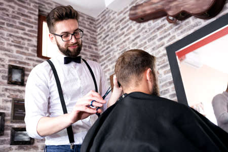 Hairdresser cutting a client's hair with scissors in a male barber shopの写真素材