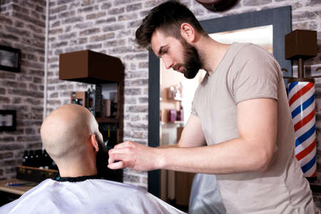 Professional Master hairdresser cuts client beard in barbershop