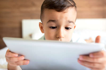 Cute little boy using his tablet and playing video games