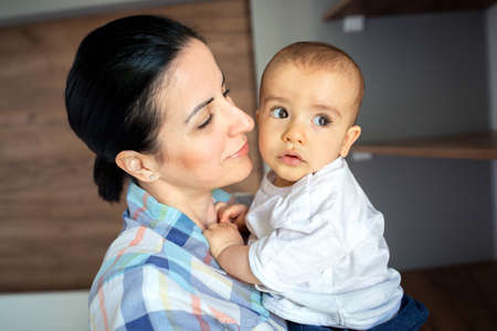 Mom holding her child with care and joy while little one seems to be distracted by someone