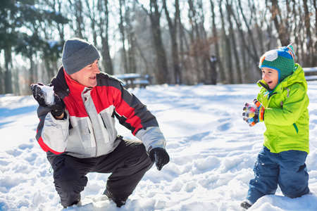 Grandfather throwing snowballs with his grandson on a bright sunny winter dayの写真素材