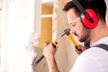 Worker carrying red protective headphones using hand demolition wall tools