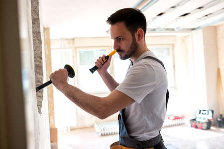 Carving a hole in the wall with pointed chisel and a hammerの写真素材