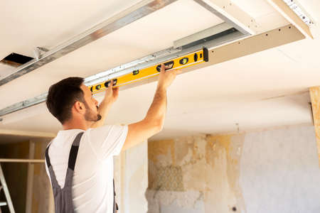 House renovation worker checking the alignment of a ceiling with a water bubble level tool