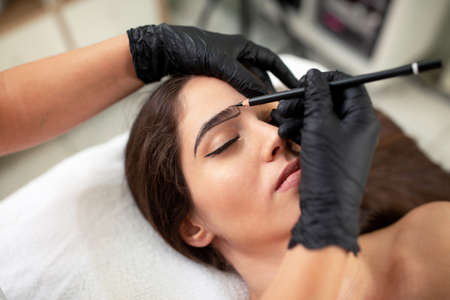 Cosmetician preparing to make a legit appearance of naturally full brows on the face of a pretty...