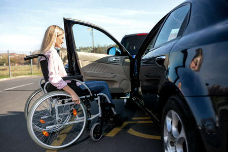 Woman with loss of leg function in the wheelchair attempting to make it to the drivers position of her carの写真素材