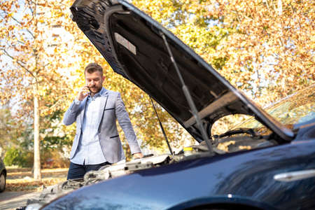 Attractive young upset man making a call while his car broke down on vacation