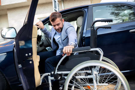 Young handicapped man reaching for his wheelchair in the handicapped zone