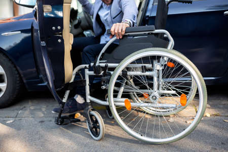 Young handicapped man reaching for his wheelchair in the handicapped zone