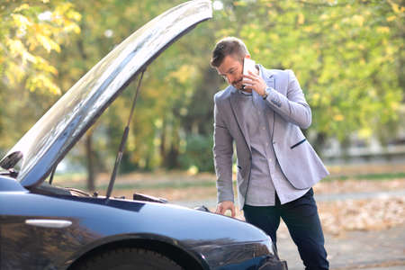 Man looking under the hood of the car trying to figure out what went wrongの写真素材