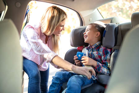 Cute little boy sitting in the child seat and his mother, preparing for the driveの写真素材