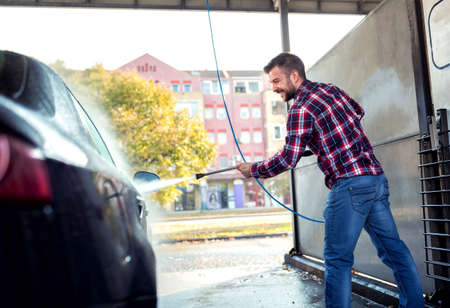 Guy washing his car observed from the back side, stop light, blue jeans, squared shirtの写真素材