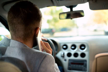 Young man being neglect while driving holding mobile phone with one hand and steering wheel with the...