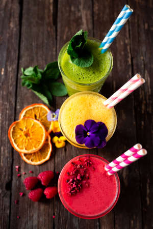 Tasty smoothies viewed from ceiling position, decorated with fruit slices, flowers and green leaves...