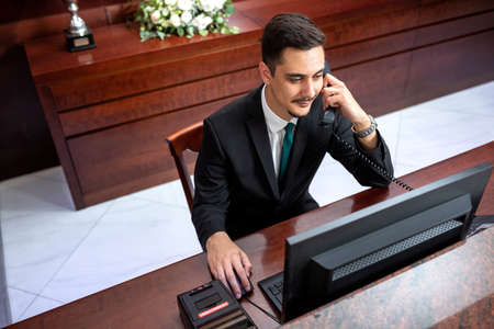 Receptionist in black suit sitting and working, reception conceptの写真素材