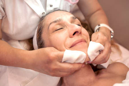 Cosmetician cleaning the surface of an older womanâ€™s face, facial skin cosmetics
