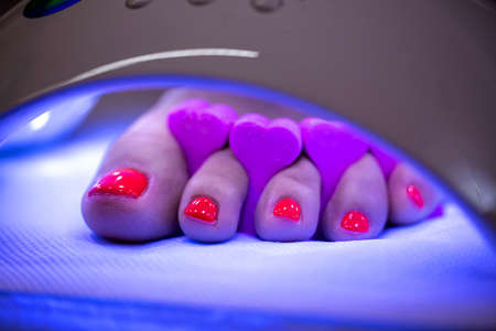 Freshly polished toenails with red nail polisher applied curing in uv led nail lamp