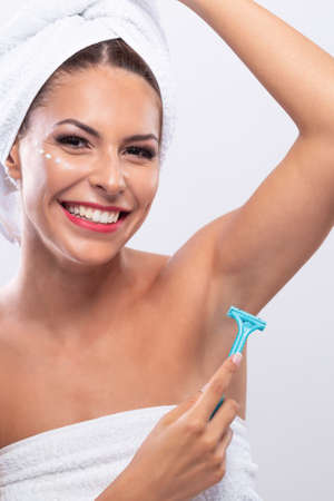 Profile of a young attractive woman with dots of face cream on her cheek shaving her armpitの写真素材