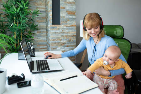 Young mother sitting and holding her child while workingの写真素材