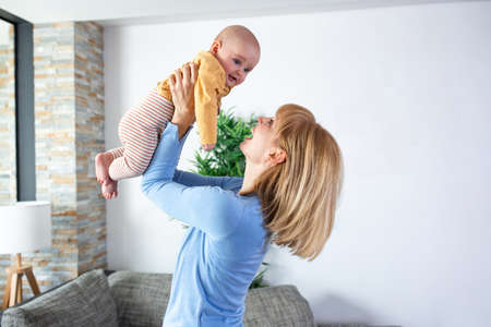 Loving mother holding her child while standing and playing tossing with him, happy faces