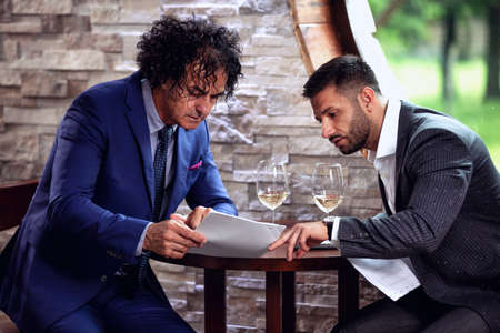 Two businessmen studying business reports on glass of wine breakの写真素材