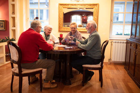 Lovers of card games sitting around the table and having funの写真素材