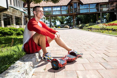 Young man chilling on the side of the road with his electric hoverboard parked right next to him, green energy conceptの写真素材