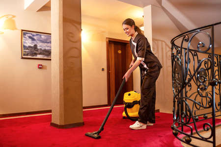 Vacuuming staff maid busy on the job, hotel service maintenanceの写真素材