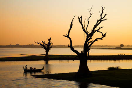 Lake by sunset with tree and boat silhouette at Amapura,  Mandalayの写真素材
