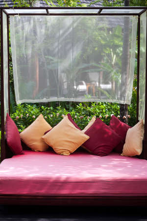 Large wooden framed canopy bed with colourful red and yellow cushionsの写真素材