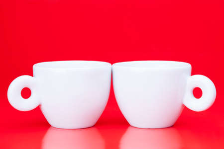 Two white coffee cups in front of a red backgroundの写真素材