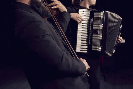 Detail of hands playing an accordion instrument and a violin on black background