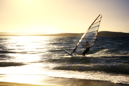 summer sports: windsurfer speeding fast against the sunsetの写真素材