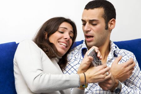 young couple watching tv and fighting to get the remote controlの写真素材