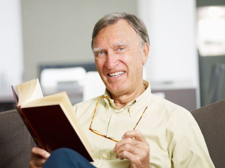 senior man reading book at home and looking at camera. Copy spaceの写真素材