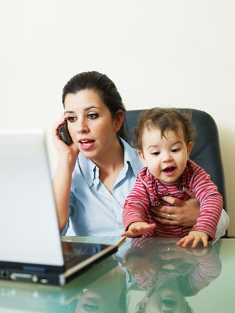 stressed business woman in office, holding her little girl while talking on mobile phone. Vertical shape, Copy spaceの写真素材