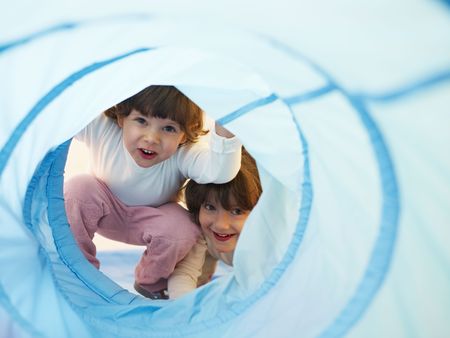 two 2-3 years old girls peeking from blue toy tunnel. Horizontal shape, Copy spaceの写真素材
