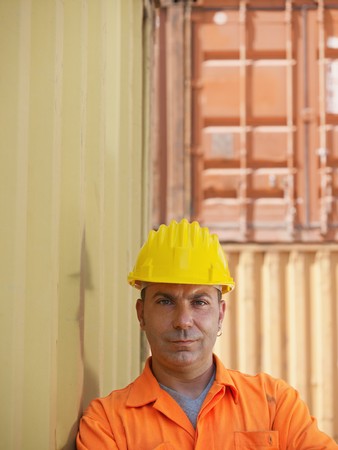 portrait of mid adult worker leaning on cargo container and looking at camera. Vertical shape, front...