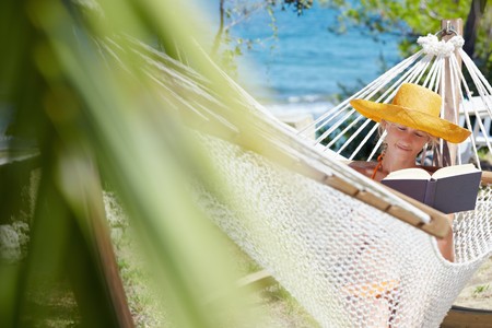 mid adult woman with orange hat reading book on hammock. Front view, Horizontal shape, copy spaceの写真素材
