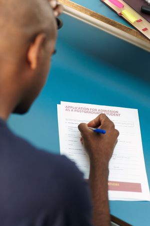 young adult african-american college student filling application form for master degree in library. Vertical shape, rear view, selective focus, head and shouldersの写真素材