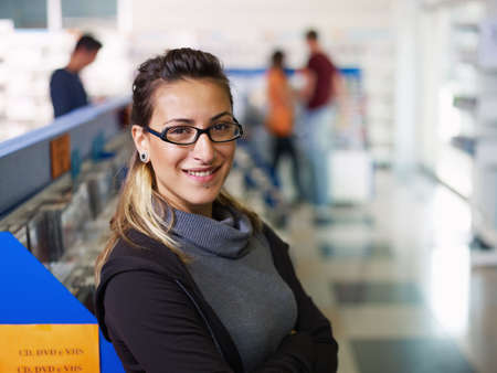 caucasian salesclerk looking at camera with arms folded in music shop, with customers in background. Horizontal shape, front view, waist up, copy spaceの写真素材