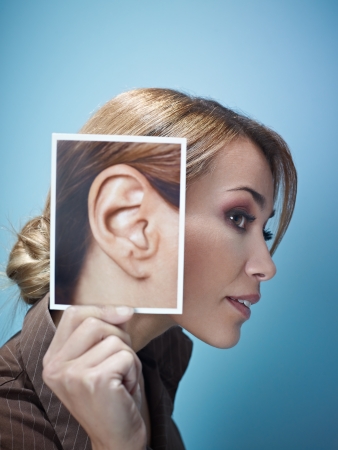 mid adult business woman holding photo of her ear on blue background. Vertical shape, side view, head and shoulders, copy spaceの写真素材