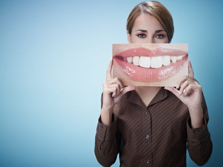 mid adult business woman holding photo of toothy smile on blue background. Horizontal shape, front view, waist up, copy spaceの写真素材